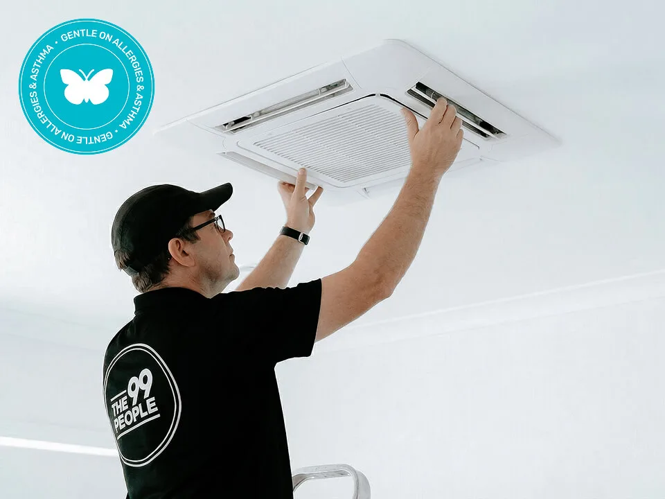 A technician wearing a black cap and shirt works on a cassette air conditioning unit. A blue "Gentle on Allergies" certification badge appears in the top left corner.