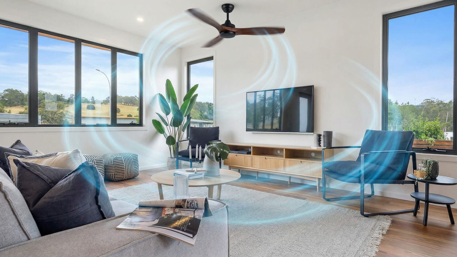 Modern living room with a freshly cleaned ceiling fan creating visible airflow patterns, featuring large windows, a TV, indoor plants, and contemporary furniture—highlighting the benefits of regular ceiling fan cleaning.