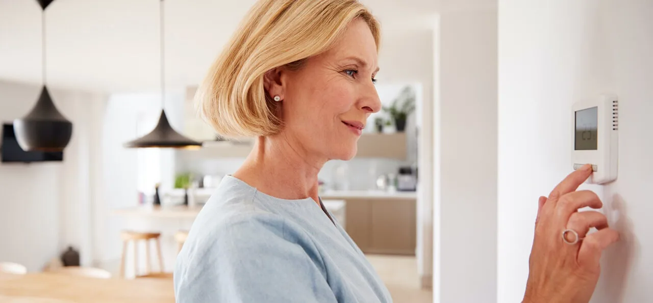 A woman stands in a modern kitchen adjusting a wall-mounted thermostat.